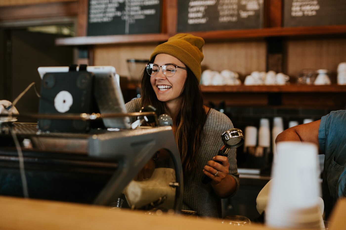 Een vrouw is met een lach aan het werk in een koffiezaak